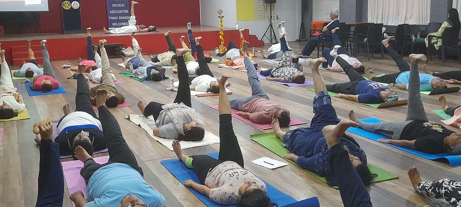 Group yoga class guided by Suruchi Mittal — students lying on mats with arms raised